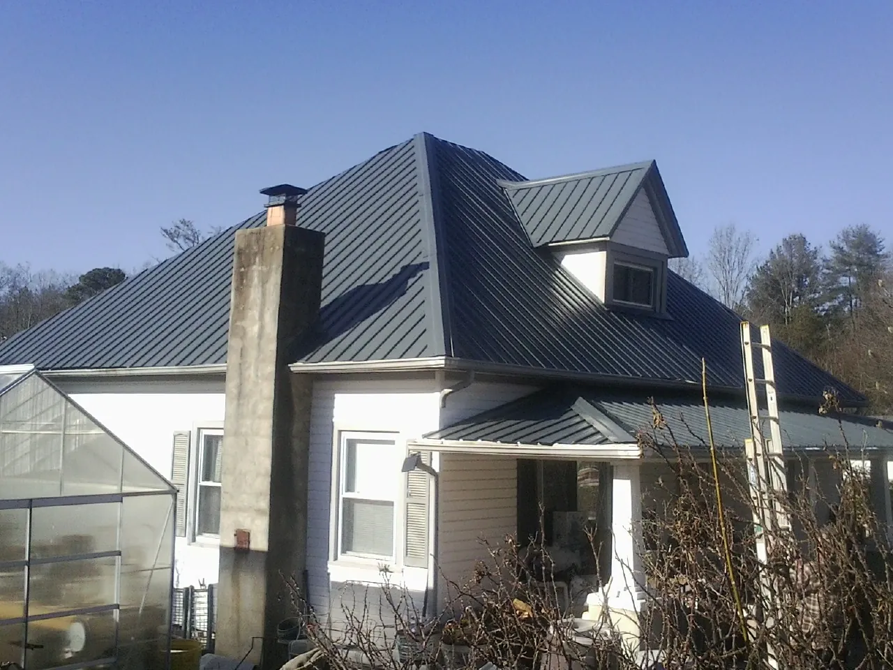 Dark blue standing seam metal roof on a white farmhouse with dormer — Slate & Tile Roof Repair by Roofing Brothers in Laotto