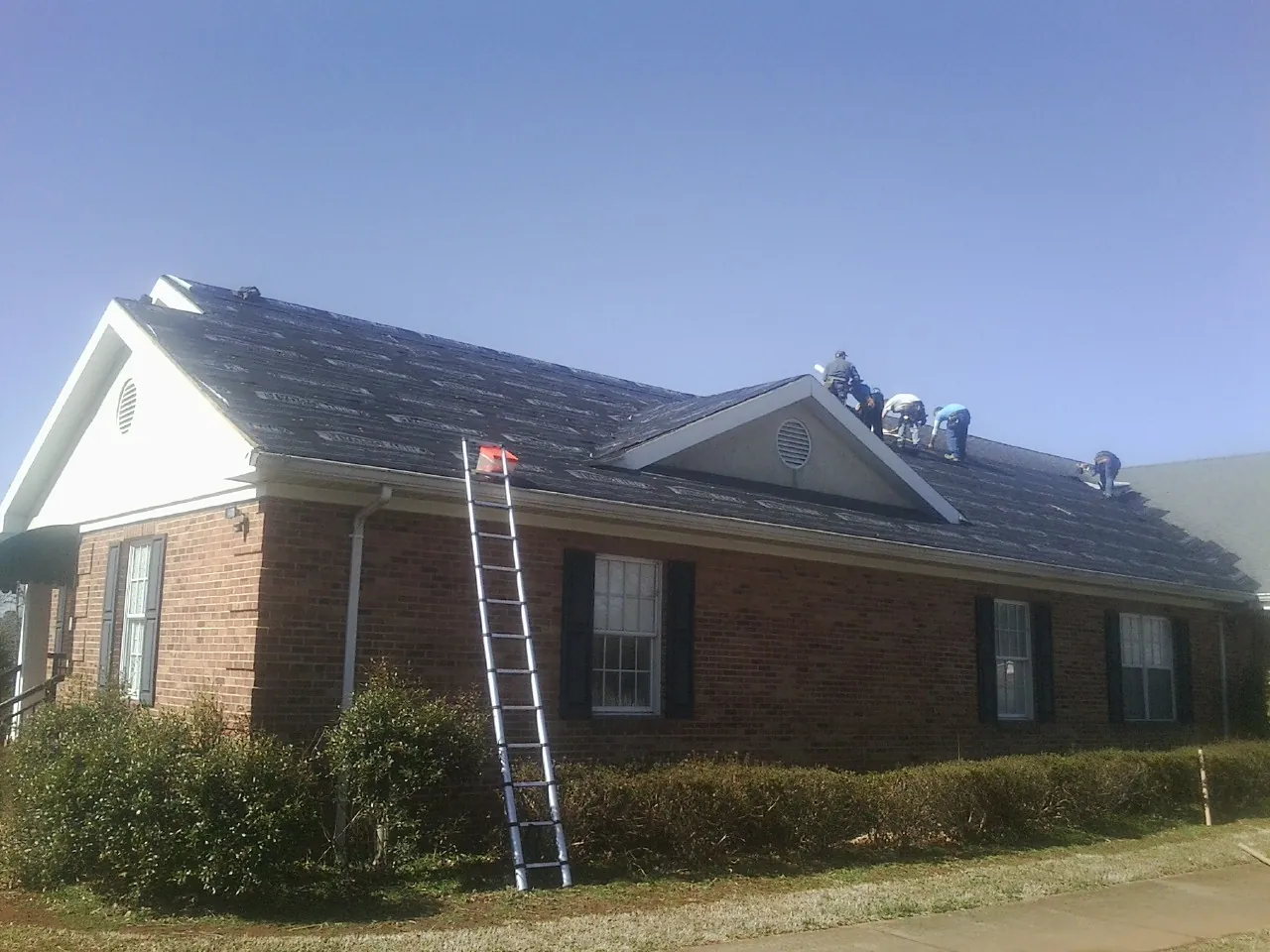 Crew tearing shingles off a brick ranch roof with a ladder set — Emergency Roof Repair work by our crew in Laotto