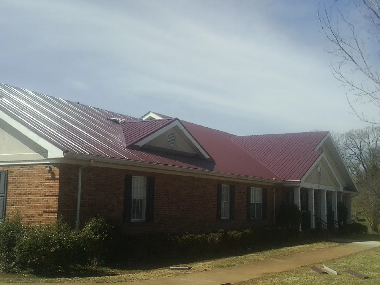 Red metal roof with gabled entries on a long brick building, from a Hail Damage Roof Repair job in Laotto