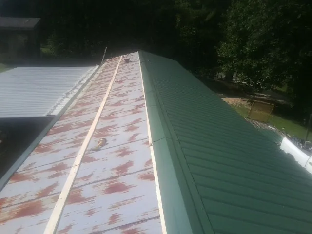Old rusted panels beside newly installed green metal roofing — Wind Damage Roof Repair by Roofing Brothers in Laotto