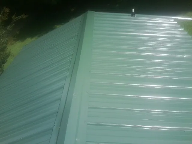 New green metal panels meeting at the ridge of a roof — Flat Roof Repair work by our crew in Laotto