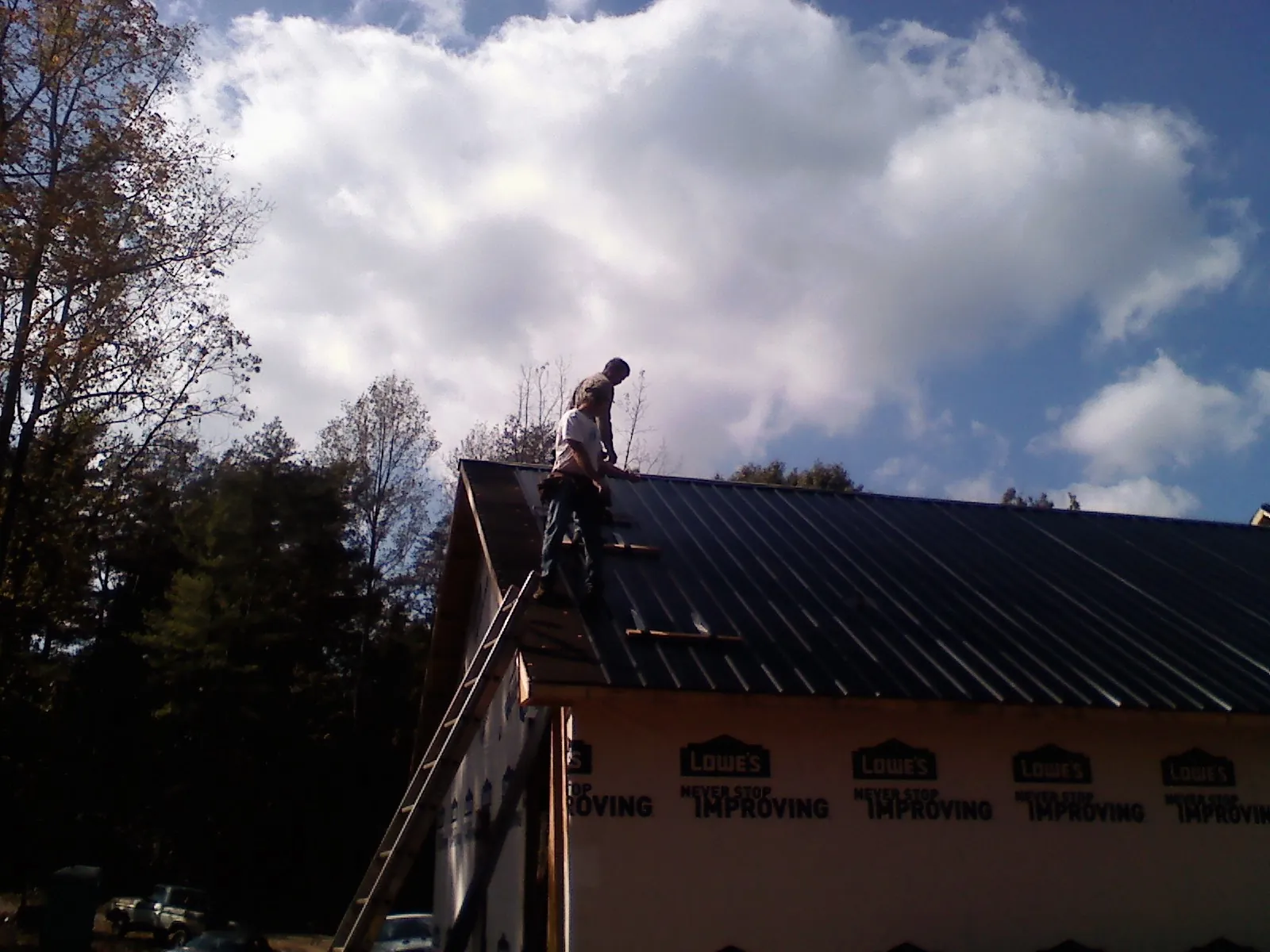 Roofer fastening dark metal panels high against a cloudy sky, from a Roof Inspection job in Laotto
