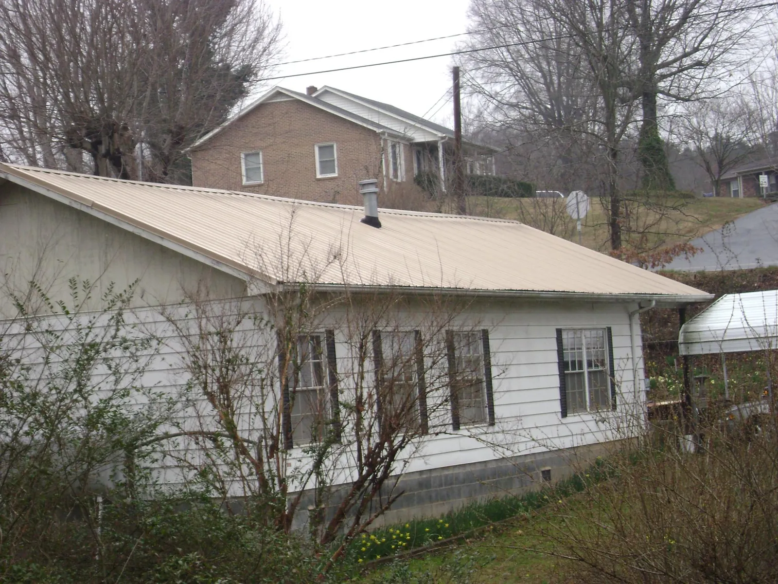 Tan metal roof on a white sided house set into a hillside — Commercial Roofing by Roofing Brothers in Laotto