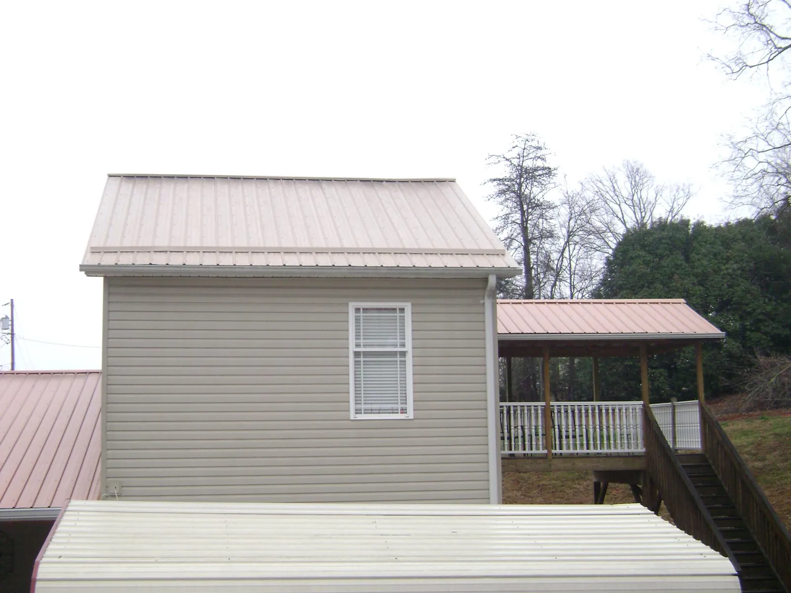 Tan metal roofs on a two story addition and attached porch, from a Roof Replacement job in Laotto